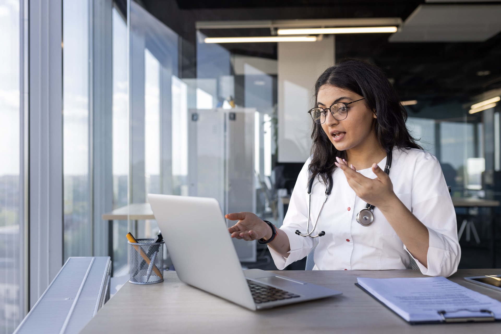 Doctor conducting online consultation via laptop in modern office with natural lighting
