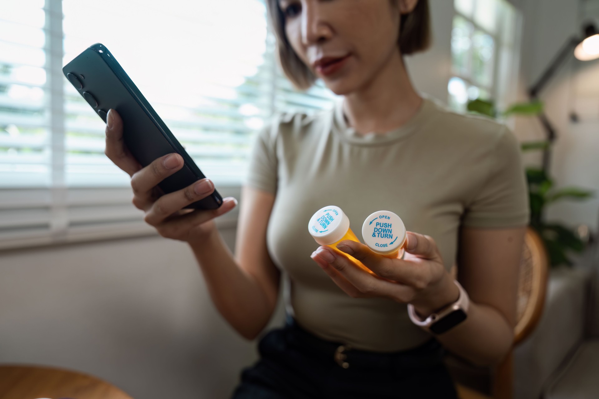Woman Checking Prescription Pills on Smartphone for Healthcare Information in Modern Home Setting